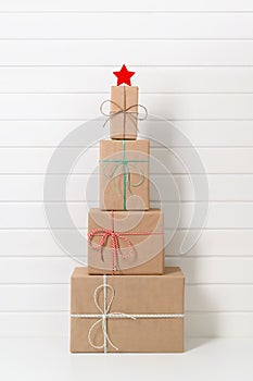 Alternative Christmas tree made from gift boxes with a white star on the background of a white wooden wall.