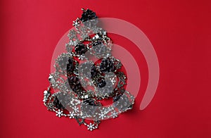 Alternative Christmas tree made of shiny garland and cones on red. Space for wishes. Holiday card. Top view. Happy New Year