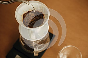 Alternative coffee brewing v60 closeup. Barista making filter coffee on brown background. Pouring hot water from steel kettle in