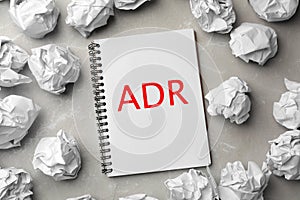 Alternative dispute resolution. Notebook with abbreviation ADR surrounded by paper balls on light grey table, flat lay