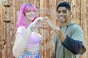 Alternative diverse couple hanging out together smiling and standing against a rusted background wall and holding hands in heart