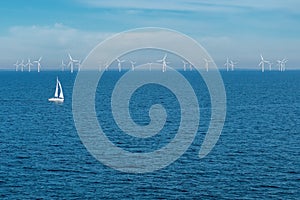 Alternative energy - row of offshore wind turbines and yacht at sea, green energy windmill generators at sea