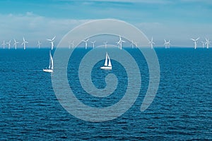 Alternative energy - row of offshore wind turbines and yachts at sea, green energy windmill generators at sea