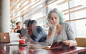 Alternative girl with green hair is sitting against group of multi ethnic people that working together by the table