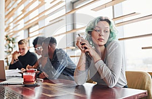 Alternative girl with green hair is sitting against group of multi ethnic people that working together by the table