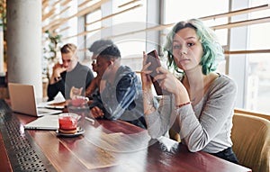 Alternative girl with green hair is sitting against group of multi ethnic people that working together by the table