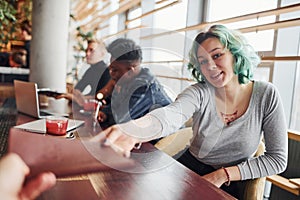 Alternative girl with green hair is sitting against group of multi ethnic people that working together by the table