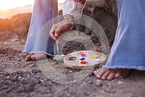 Alternative hippy barefoot style caucasian woman painting mandala on stones on the ground - feeling with nature and outdoor