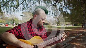 An alternative man concentrated while playing guitar at park