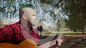 Alternative man sitting at park and singing while playing guitar