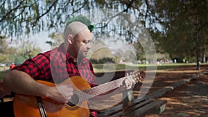 Alternative man sitting at park and singing while playing guitar