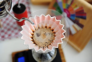 Alternative manual brewing. Pouring water in coffee in pink origami dripper with paper wave filter. Top view, close up