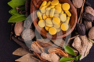 Alternative medicine concept. Top view Close-up shot of yellow ayurvedic medicines in a wooden spoon and different herbs on black