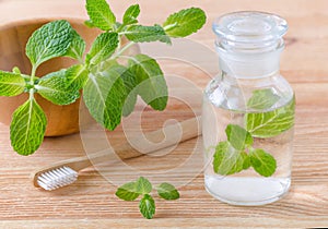 Alternative natural mouthwash bottle with mint and wood toothbrush closeup on wooden