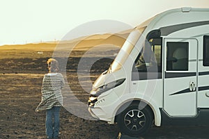 Alternative tourist vanlife concept with standing woman in back view near a big camper van motornohome enjoying the freedom and