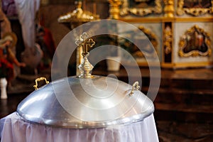 Aluminium church font, large bowl, with golden cross and saint water for the baptism of babies in Orthodox Church temple