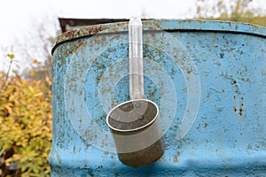 aluminum bucket hangs on a metal blue barrel in the autumn garden