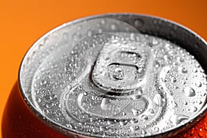 Aluminum can of beverage covered with water drops on orange background