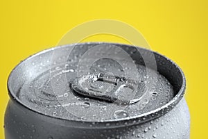 Aluminum can of covered with water drops on yellow background, closeup