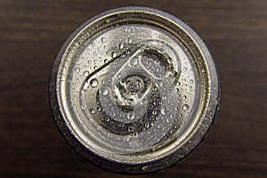 Aluminum can with water drops on the lid, on a dark colored background, top view. Beer can or soft drink