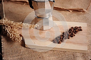 Aluminum coffee cup and coffee beans on wooden cutting board on burlap sack and wheat background