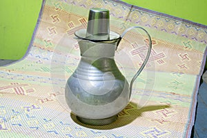 An Aluminum water jag with a stainless steel mug or glass on a mat. old fashioned water pot. photo