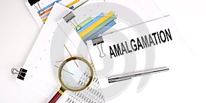 AMALGAMATION text on white paper on the light background with charts paper