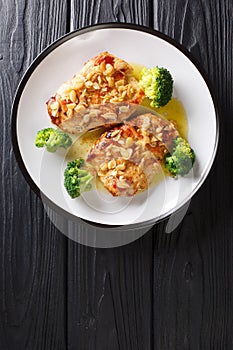 Amandine chicken fillet in almond sauce and broccoli close-up on a plate. Vertical top view