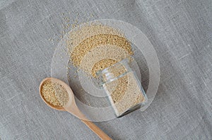 Amaranth seeds from small glass bottle and pigweed seeds in spoon on linen background. Fabric background
