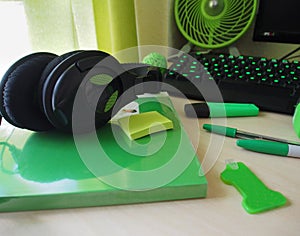 Amateur green. A computer, headphone, pens, marker on wood table