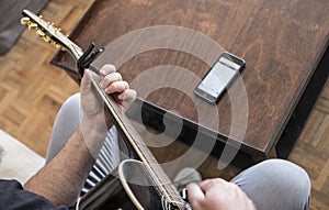 Amateur guitarist reading chords on mobile phone