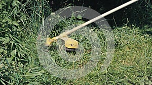 Amateur man cutting grass by petrol brushcutter or grass trimmer with star-shaped three steel knife blades and grass