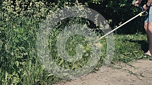 Amateur man cutting grass by petrol brushcutter or grass trimmer with star-shaped three steel knife blades and grass