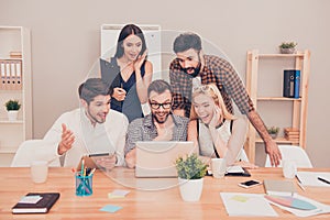 Amaze news! photo of happy young workers sitting and looking at laptop