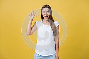 Amaze young woman pointing to one side with her finger while opening her mouth against a yellow background