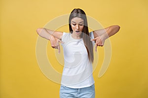 Amaze young woman pointing to one side with her finger while opening her mouth against a yellow background