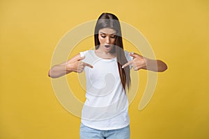 Amaze young woman pointing to one side with her finger while opening her mouth against a yellow background