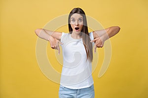 Amaze young woman pointing to one side with her finger while opening her mouth against a yellow background