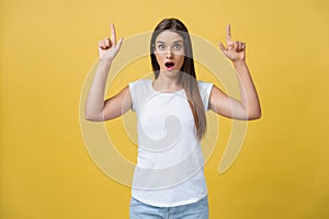 Amaze young woman pointing to one side with her finger while opening her mouth against a yellow background