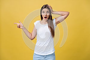 Amaze young woman pointing to one side with her finger while opening her mouth against a yellow background