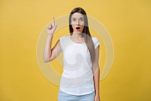 Amaze young woman pointing to one side with her finger while opening her mouth against a yellow background