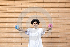 Amazed African-American man holding blue and pink donuts in his hands, wearing a white T-shirt