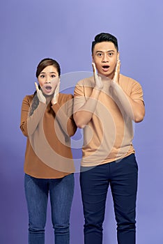 Amazed asian couple expressing shock, purple studio background