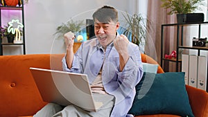 Amazed asian man use laptop computer, receive good news message, shocked by victory, celebrate win