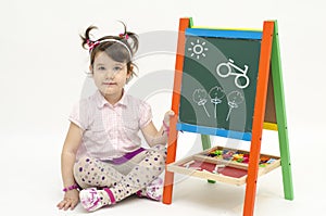 Amazed baby girl draw flowers and bike on black board with chalk