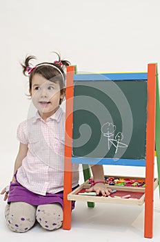 Amazed baby girl draw flowers on black board with chalk