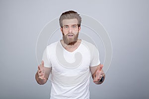 Amazed bearded man dressed in a white T-shirt looking into the camera with wide-open eyes