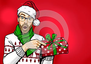 Amazed bearded man in glasses  and Santa hat with open mouth showing gift box. Emotions and advertisement. Surprised men.