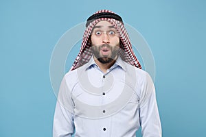 Amazed bearded young arabian muslim man in keffiyeh kafiya ring igal agal casual clothes  on pastel blue photo