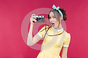 Amazed beautiful pinup girl in yellow dress holding old camera